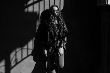 Fototapeta na wymiar Outdoor portrait of a young elegant woman in hard light with shadows of urban wearing trendy black jacket with incredible makeup. Black and white photography. Close up. Text space.