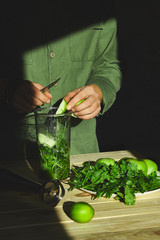 Process of preparing green detox smoothie with blender, young man  cut apples and put, cooking healthy smoothie with fresh fruits and greens spinach. Lifestyle detox concept. Vegan drinks..