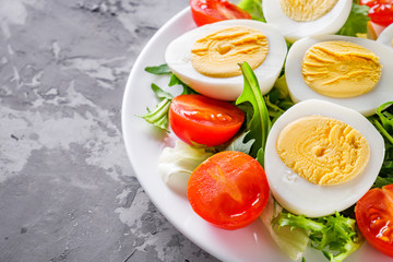salad with boiled chicken eggs and cherry tomatoes on a stone background