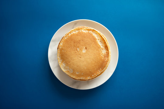 Fresh pancakes on a white dish. Classic blue background. 2020