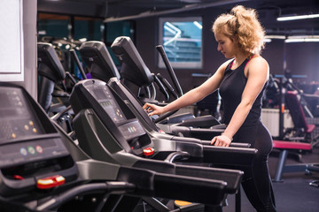 Fototapeta na wymiar Girl in black sportswear on a treadmill in the gym. Girl presses a button on the screen
