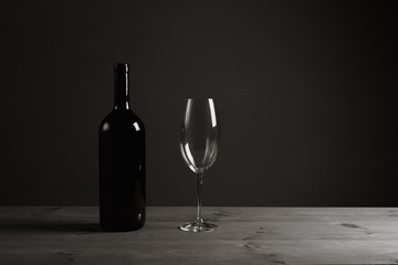 Black bottle of wine and a glass. A bottle of wine stands on a table, a bottle on a gray background...
