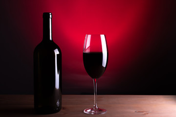 Black bottle of red wine and a glass. A bottle of wine stands on a table, a bottle on a gray background and a wooden table. Red vine.