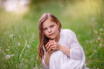 girl child holding a chicken in her hands sitting on the green grass, spring