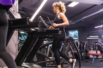 Fototapeta na wymiar A girl in a black sports uniform runs on a treadmill in a sports hall.