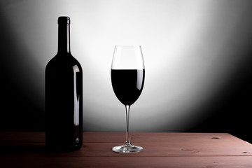 Black bottle of red wine and a glass. A bottle of wine stands on a table, a bottle on a gray background and a wooden table.