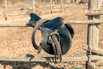 A leather saddle of a horseman on a rustic fence against a background of dead grass.