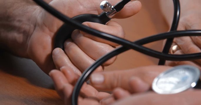 Close-up detail shot of hands of an elderly couple. Husband takes care of his wife by measuring her blood pressure using a mechanical tonometer on a brown wooden table at home. 4k 50fps slow motion