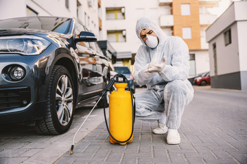 Man in protective suit with mask disinfecting car tires, prevent infection of Covid-19 virus coronavirus,contamination of germs or bacteria. 