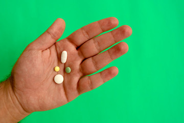 Man's hand with different pills on green background with copy space. Top view. Many different tablets in hand.