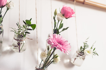 Beautiful flowers hang on white wall. Old glass jars are reused as flower vases. DIY Home natural Decor