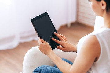 Naklejka premium A young girl sits in chair with tablet and pays bills, online purchases, payment for goods during quarantine, A young girl undergoes online training, online training during quarantine, work from home