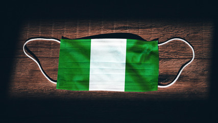 Nigeria National Flag at medical, surgical, protection mask on black wooden background. Coronavirus...