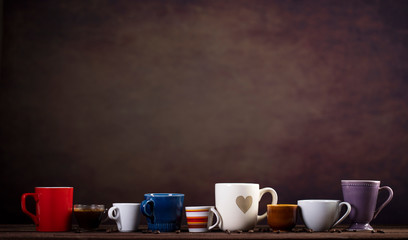 Collection of different cups on wooden table and dark brown background with copy space