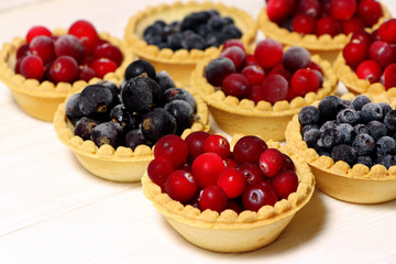 Tasty tartlets with different berries,cranberries,bilberry,blackcurrant . Berry tartlets. Cake with berries. Dessert with berries. Wooden background. Healthy food, vitamins.