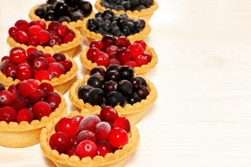 Tasty tartlets with different berries,cranberries,bilberry,blackcurrant . Berry tartlets. Cake with berries. Dessert with berries. Wooden background. Copy space. Healthy food, vitamins.