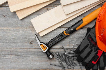 Carpentry tools hammer, nails, wooden bars, helmet and gloves on a gray wooden table