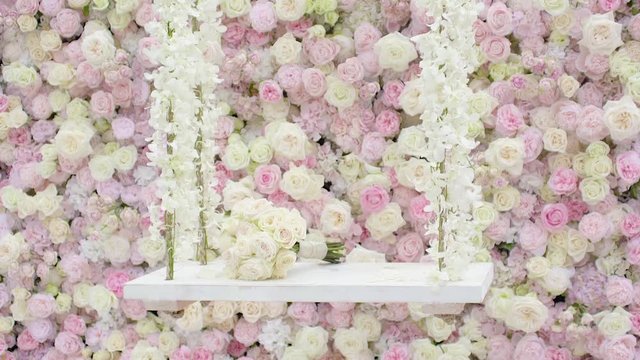 A bouquet of flowers placed on a white swing adorned with flowers with flower wallpaper in background 