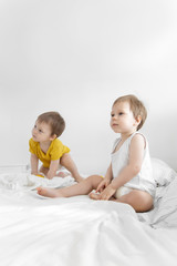 Small twins sit and play with toys on bed. Babies twins sit down in Bed. Fashion image of baby and family