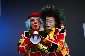 Two clowns a man and a woman with bright makeup in colored costumes speak in a megaphone to make an...