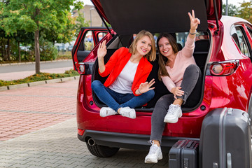 Two girls in trunk of red car posing for camera