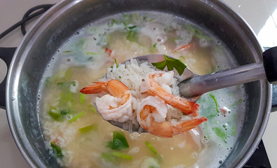Shrimp porridge in ladle while cooking and pan background.