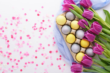 Paschal composition of Easter eggs and purple tulips on white background with pink confetti