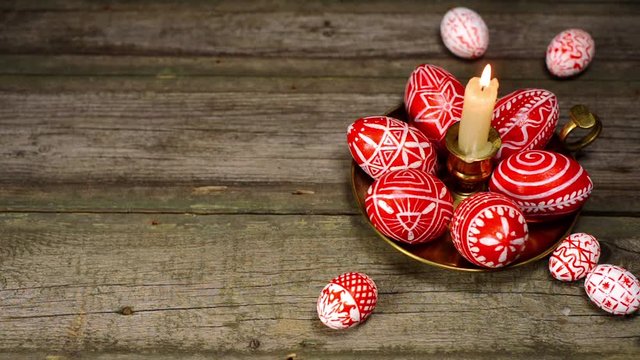 Easter eggs rolled up to candlestick with burning candle and red eggs with folk white pattern, which stand on white background. Ukrainian eggs pisanka and krashanka.