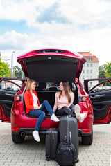 Two young girls rest from packing luggage in car