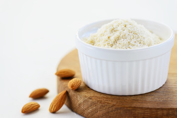 Almond flour in a white bowl on a wooden board. Gluten free food.