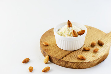 Almond flour in a white bowl with almonds on a wooden board. Healthy food, gluten free.
