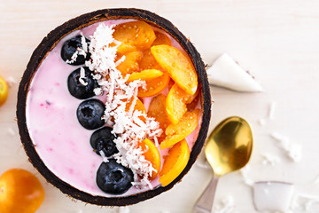 top view smoothie bowl with blueberries, physalis and coconut shavings in coconut bowl with spoon on white background