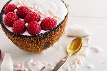 trendy dessert with whipped cream, raspberries and pastry sprinkles in coconut bowl with spoon on white background