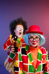 Two clowns a man and a woman with makeup in bright colored costumes are fooling around and showing a presentation