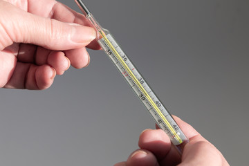 Female hands are holding a thermometer with a temperature of 39.1. Large mercury thermometer. The concept of COVID-19 colds, flu, epidemics. 