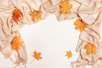 Autumn background, white wood with dry yellow autumnal season leaves of maple tree, cozy textile scarf. Copy space. Top view.