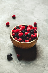 raspberries and blackberries in wood bowl on gray table, vintage