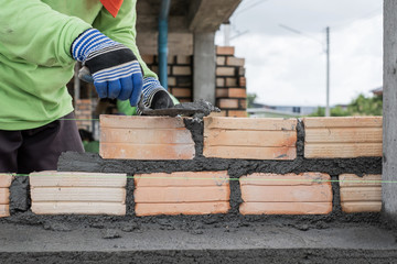 Close up of mansory bricklayer worker hand installing bricks on construction site