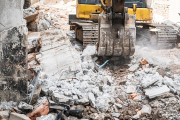 Fototapeta premium Small yellow excavator is on duty for pulling down the old buildings. Selective focus at bucket.