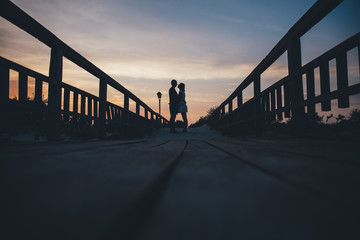 Silhouette of a couple in love at sunset on a wooden bridge.