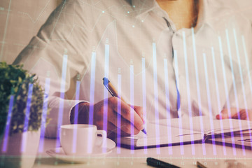 Double exposure of man's hands writing notes of stock market with forex chart.