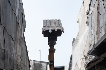 Small yellow excavator is on duty for pulling down the old buildings. Selective focus at bucket.