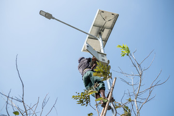 Thai young man in freestyle uniform climb bamboo wooden ladder to fix public electric light lamp.