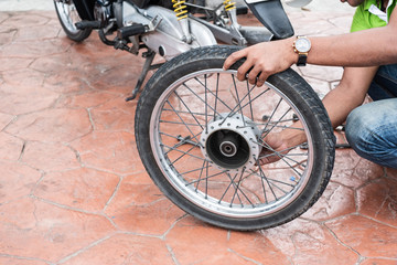 Thai yiung man is holding motorcycle wheel to repair after tire leaks or disc damage. Motorcycle repair