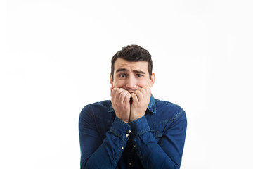 Scared and worried young man biting finger nails being afraid isolated on white background.