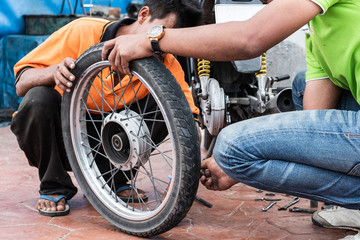 Obraz na płótnie Canvas Thai yiung man is holding motorcycle wheel to repair after tire leaks or disc damage. Motorcycle repair