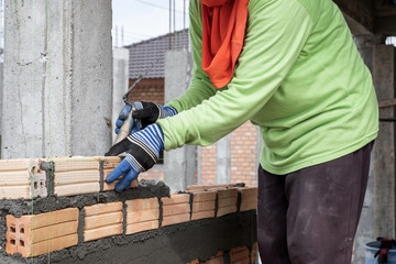 Close up of mansory bricklayer worker hand installing bricks on construction site
