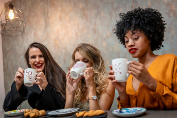 Session in a cafeteria. Three young friends having a coffee and some pastries in a cafeteria. Blonde girl, brunette girl and girl of Caribbean American origin with afro hair