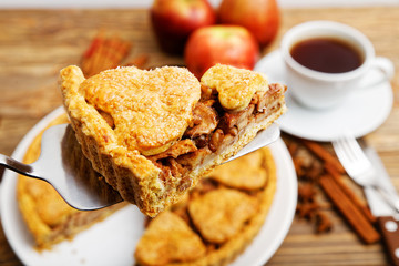 Closeup piece of homemade apple pie with cinnamon and cup of tea on wooden table. Shallow focus.
