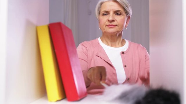 people, housework and housekeeping concept - senior woman with duster cleaning rack at home